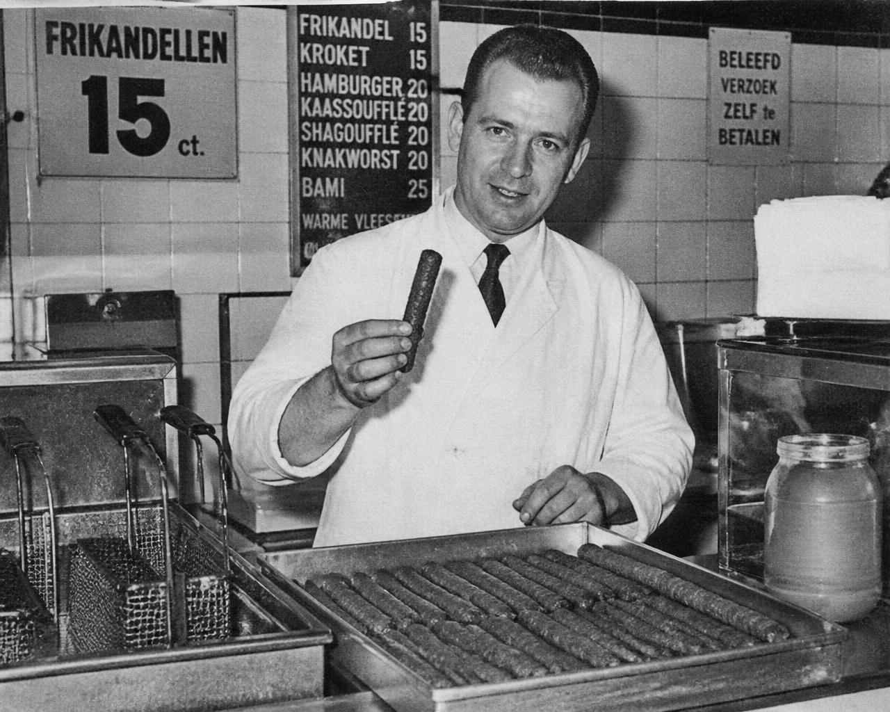 Snackbarmedewerker houdt een frikandel omhoog, jaren vijftig